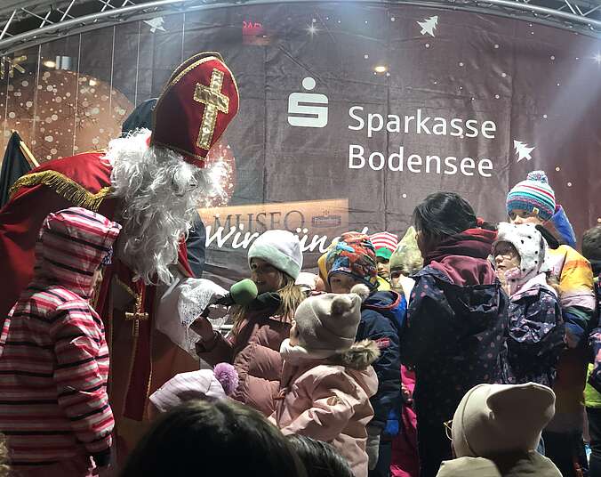 Der Nikolaus im roten Mantel steht inmitten vielen Kinder